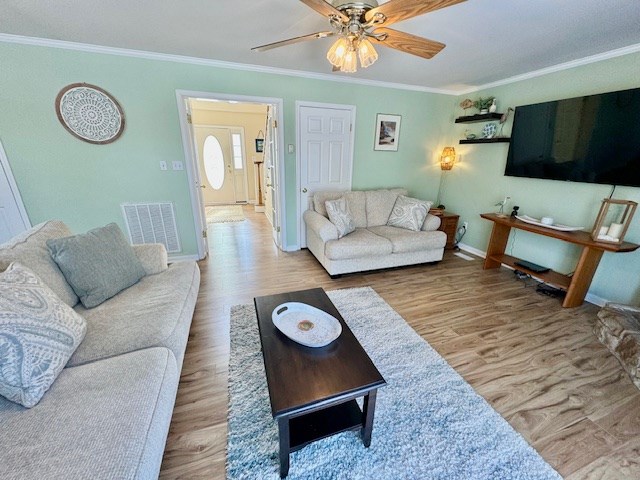 living room with wood finished floors, visible vents, and crown molding