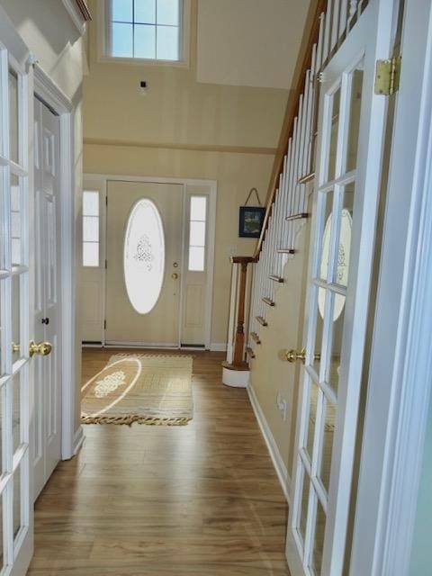 entryway featuring stairs, a towering ceiling, baseboards, and wood finished floors