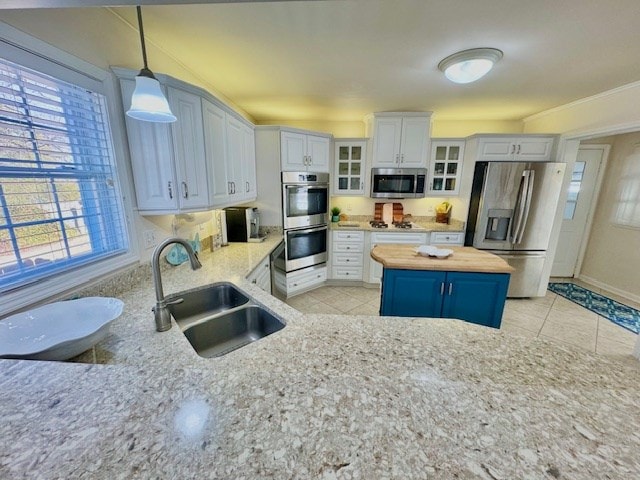 kitchen featuring wood counters, glass insert cabinets, appliances with stainless steel finishes, pendant lighting, and a sink