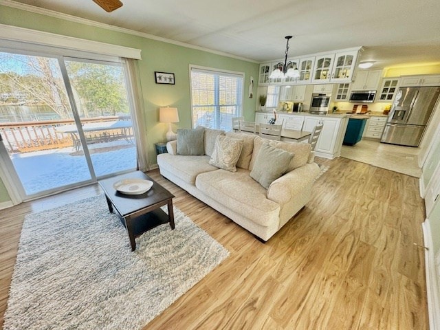 living area with light wood finished floors, ornamental molding, and an inviting chandelier