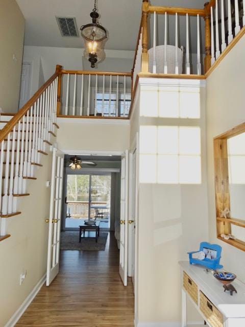 corridor with visible vents, stairway, a high ceiling, wood finished floors, and baseboards