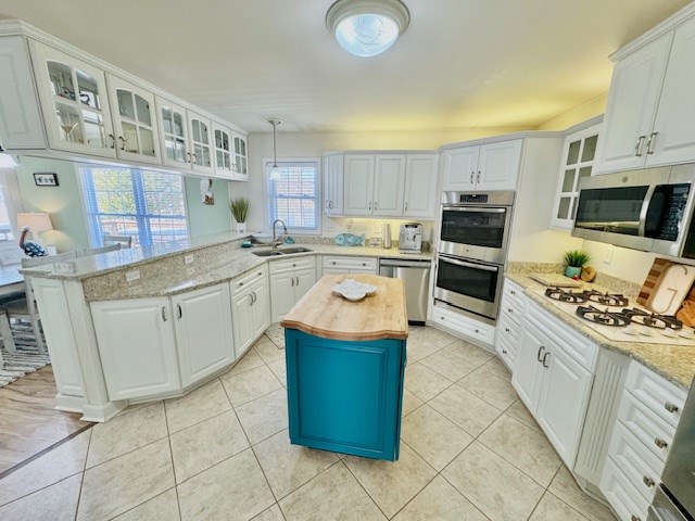 kitchen featuring a peninsula, butcher block countertops, a sink, white cabinetry, and appliances with stainless steel finishes