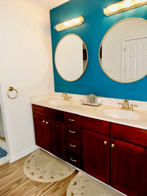 full bath featuring double vanity, wood finished floors, a sink, and baseboards