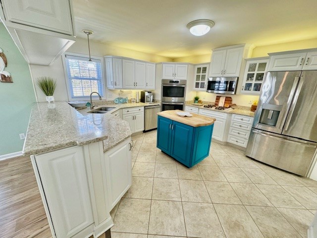 kitchen featuring stainless steel appliances, a peninsula, a sink, wooden counters, and blue cabinetry