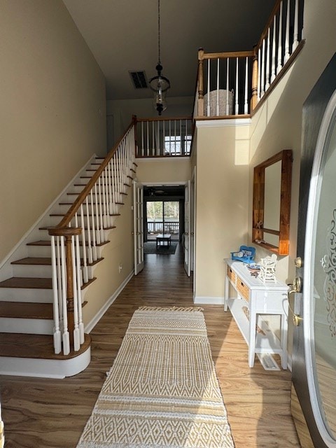 foyer entrance featuring a high ceiling, stairway, wood finished floors, and visible vents