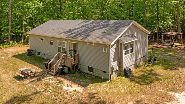 rear view of house with a view of trees, crawl space, a gazebo, and roof with shingles