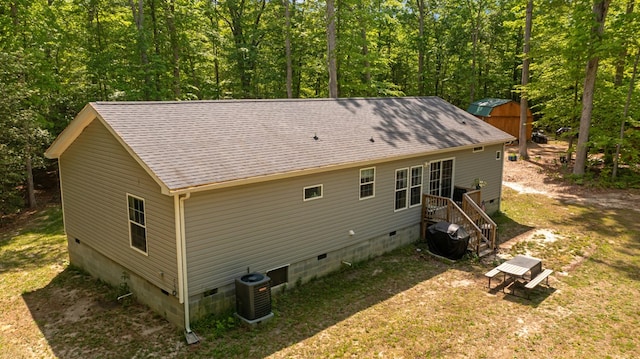 back of house featuring central air condition unit, crawl space, a view of trees, and a shingled roof