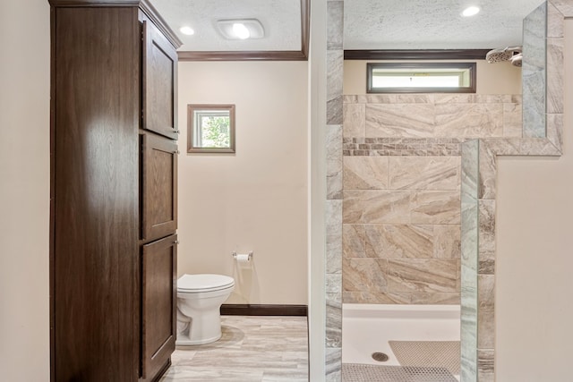 bathroom with a textured ceiling, toilet, tiled shower, and a wealth of natural light
