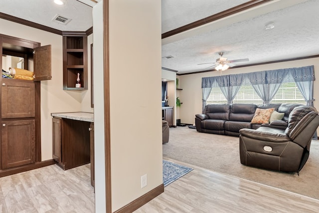 living area featuring a ceiling fan, a textured ceiling, visible vents, crown molding, and light wood finished floors