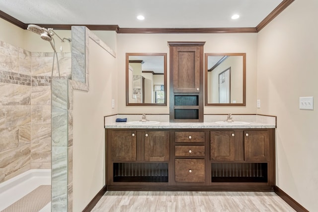 bathroom with baseboards, tiled shower, and a sink