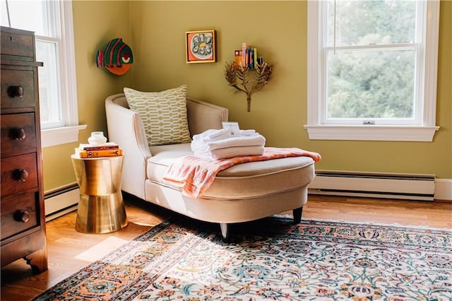 living area with a wealth of natural light, a baseboard heating unit, and wood finished floors