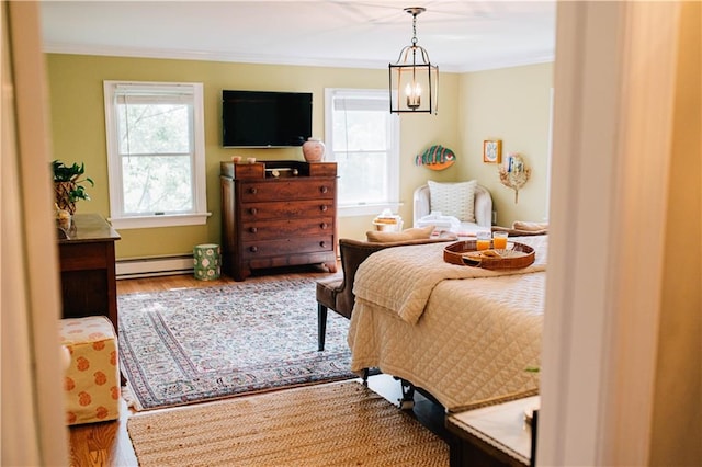 bedroom featuring baseboard heating, multiple windows, ornamental molding, and wood finished floors