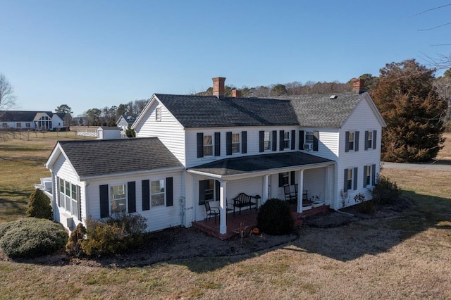 rear view of property with roof with shingles, a chimney, a lawn, and covered porch
