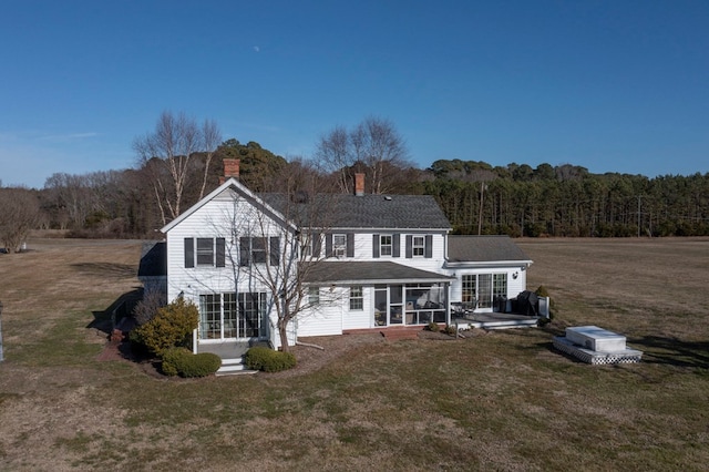 rear view of house featuring a sunroom, a view of trees, a yard, roof with shingles, and a chimney