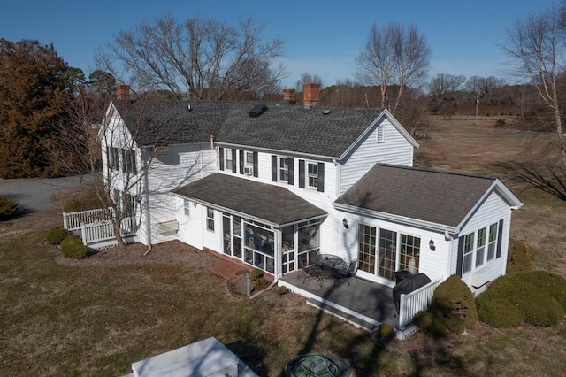 rear view of house with a sunroom, a chimney, a shingled roof, and a yard