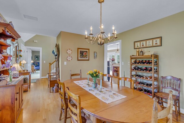 dining room featuring light wood-style floors, an inviting chandelier, vaulted ceiling, and stairs