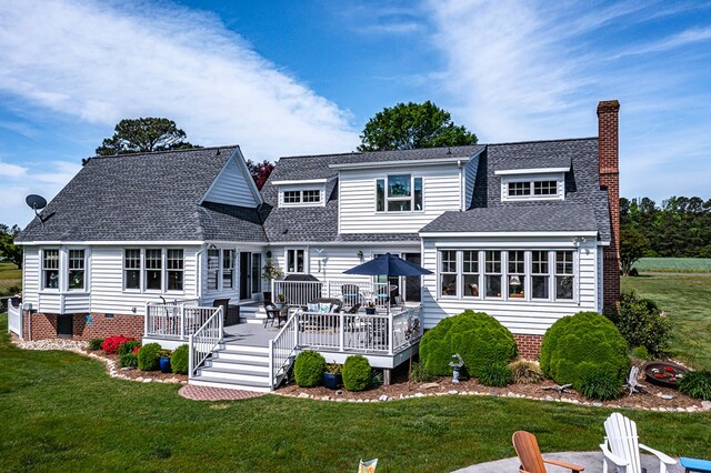 rear view of house with a yard, a deck, a chimney, and roof with shingles