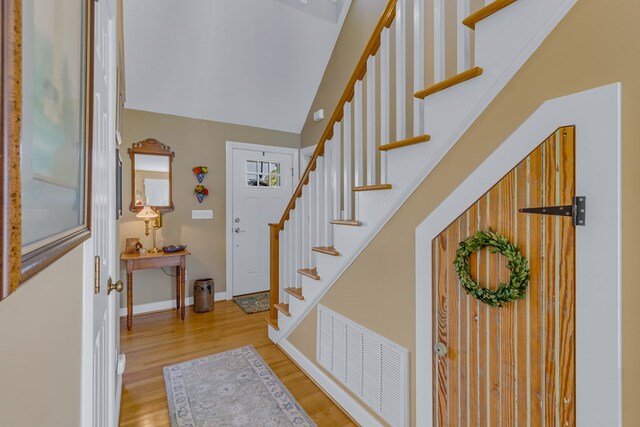 entryway featuring stairs, baseboards, wood finished floors, lofted ceiling, and visible vents