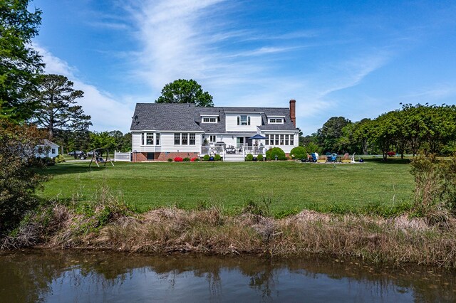 back of property featuring a lawn, a water view, a chimney, and a shingled roof
