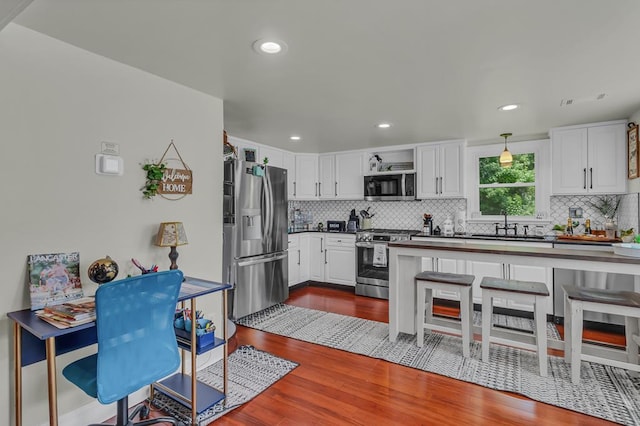 kitchen with sink, stainless steel appliances, dark hardwood / wood-style floors, decorative light fixtures, and white cabinets