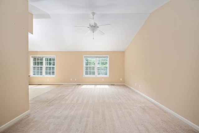 unfurnished room with ceiling fan, light colored carpet, a wealth of natural light, and vaulted ceiling