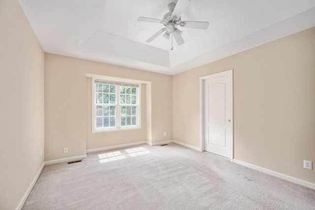 empty room featuring a tray ceiling, ceiling fan, and light colored carpet