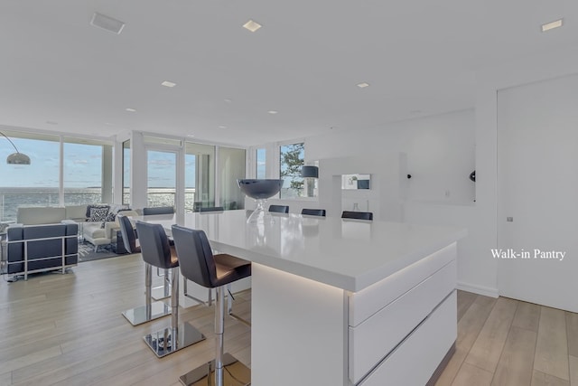 kitchen with expansive windows, a spacious island, light hardwood / wood-style floors, white cabinetry, and a breakfast bar area