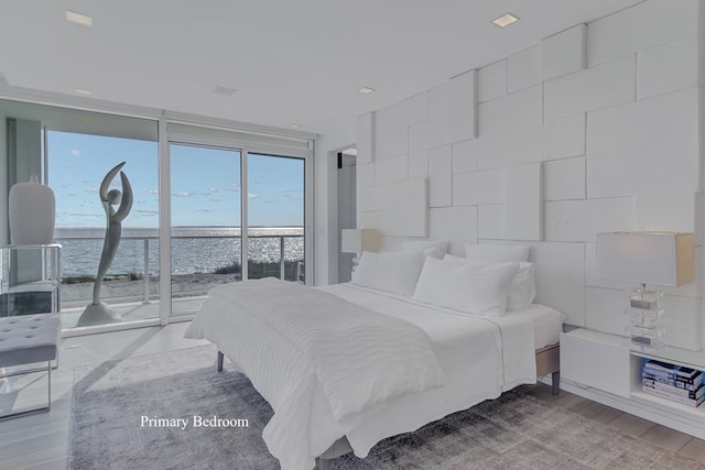 bedroom featuring access to exterior, a water view, wood-type flooring, and expansive windows