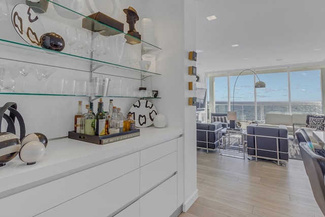 bar with white cabinets, a water view, floor to ceiling windows, and light hardwood / wood-style floors