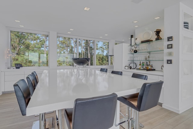 dining area with floor to ceiling windows, bar, light hardwood / wood-style flooring, and a wealth of natural light