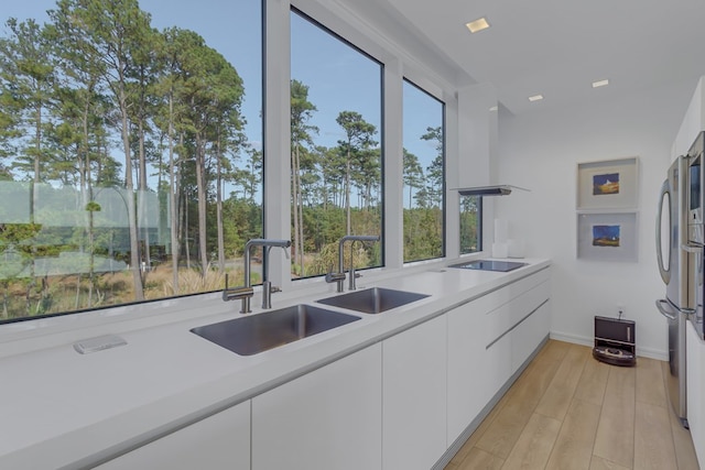 kitchen featuring sink, stainless steel fridge, light wood-type flooring, black electric cooktop, and white cabinetry