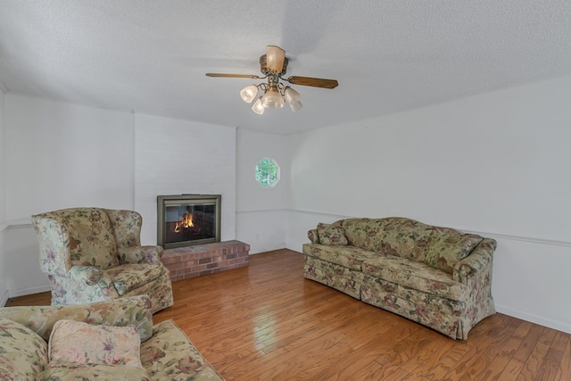 living room with ceiling fan, a fireplace, light hardwood / wood-style floors, and a textured ceiling