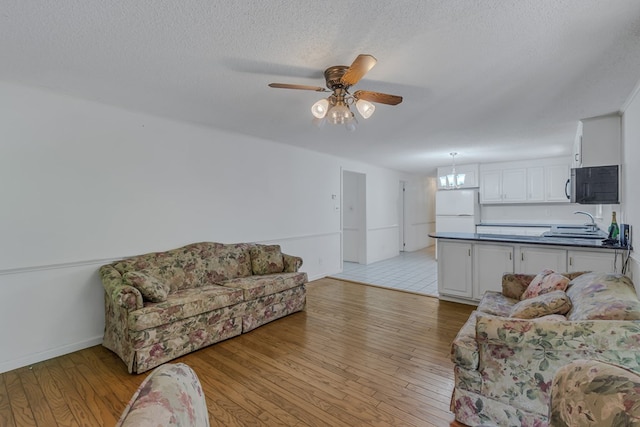 living room with ceiling fan with notable chandelier, light hardwood / wood-style floors, sink, and a textured ceiling