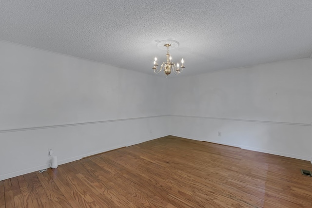 empty room featuring hardwood / wood-style flooring, a textured ceiling, and a notable chandelier