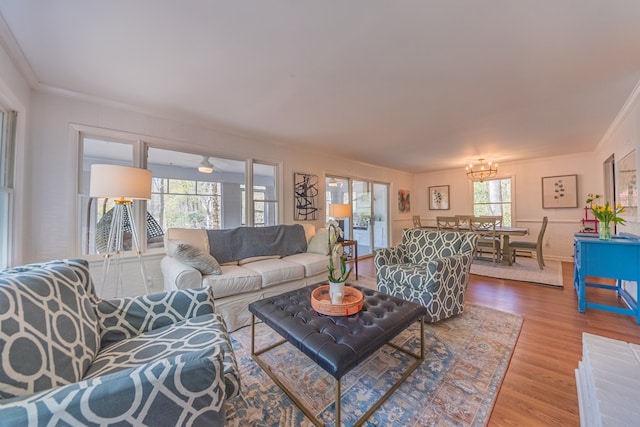 living room with wood-type flooring, plenty of natural light, an inviting chandelier, and ornamental molding