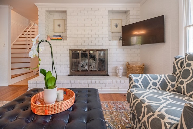 living room with ornamental molding, a brick fireplace, and hardwood / wood-style floors