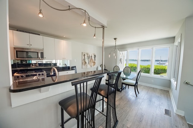 1032 Fishing Bay Rd, Deltaville, VA 23043 - kitchen with appliances with stainless steel finishes, a kitchen bar, dark countertops, light wood-style flooring, and white cabinets