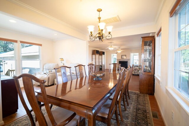 dining space featuring ornamental molding, ceiling fan with notable chandelier, wood finished floors, a fireplace, and baseboards