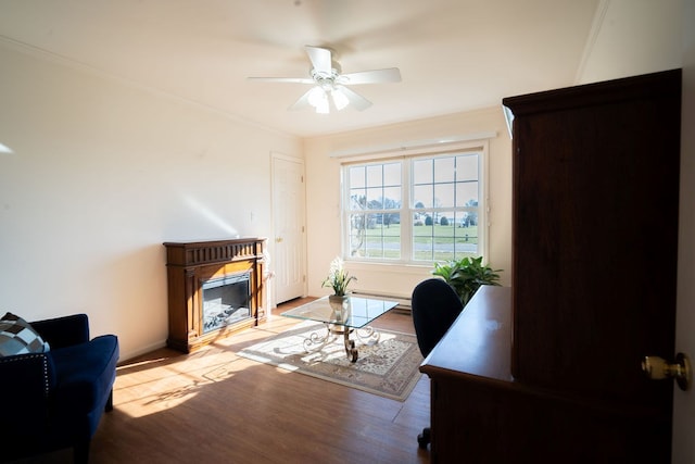 office with a ceiling fan, wood finished floors, a glass covered fireplace, crown molding, and baseboards