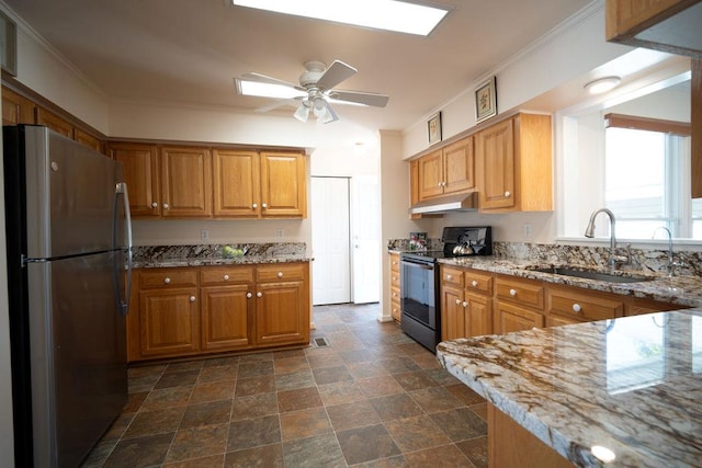 kitchen with light stone counters, black / electric stove, freestanding refrigerator, a sink, and under cabinet range hood