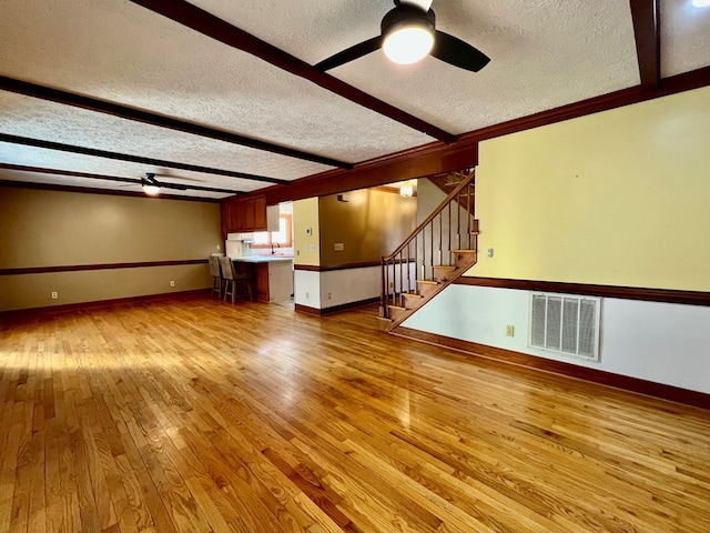 unfurnished living room featuring sink, ceiling fan, light hardwood / wood-style floors, a textured ceiling, and beamed ceiling