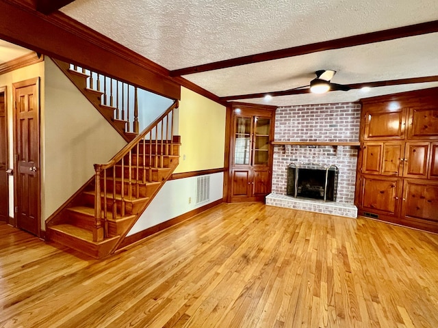 unfurnished living room with a brick fireplace, light hardwood / wood-style flooring, a textured ceiling, ornamental molding, and beamed ceiling