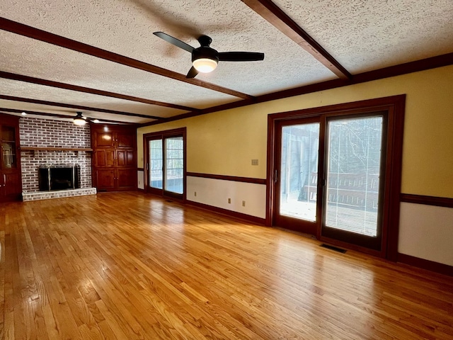 unfurnished living room featuring a brick fireplace, a textured ceiling, light hardwood / wood-style floors, and ceiling fan