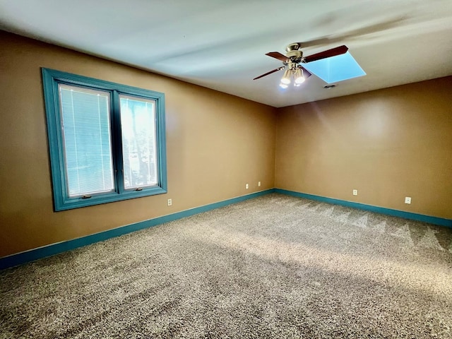 carpeted empty room featuring ceiling fan and a skylight