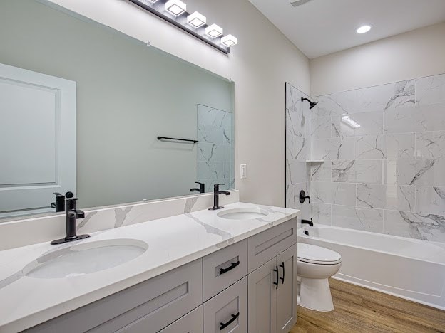 full bathroom featuring vanity, wood-type flooring, tiled shower / bath combo, and toilet