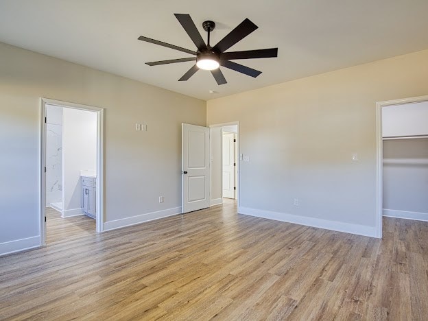 unfurnished bedroom featuring connected bathroom, light hardwood / wood-style flooring, a spacious closet, and ceiling fan