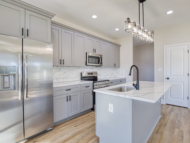 kitchen featuring sink, stainless steel appliances, an island with sink, pendant lighting, and decorative backsplash