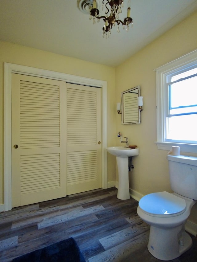 half bathroom with toilet, a sink, wood finished floors, a chandelier, and baseboards