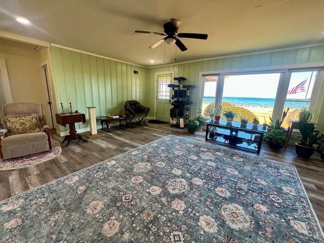 living area featuring a beach view, a ceiling fan, wood finished floors, a water view, and crown molding