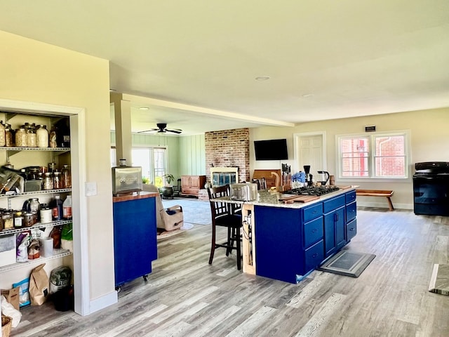 kitchen with a breakfast bar, ceiling fan, light wood-type flooring, blue cabinetry, and a fireplace